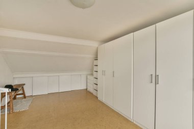 Bu fotoğrafta duvarında beyaz dolaplar ve dolaplar olan boş bir oda en üst kattan çekiliyor.