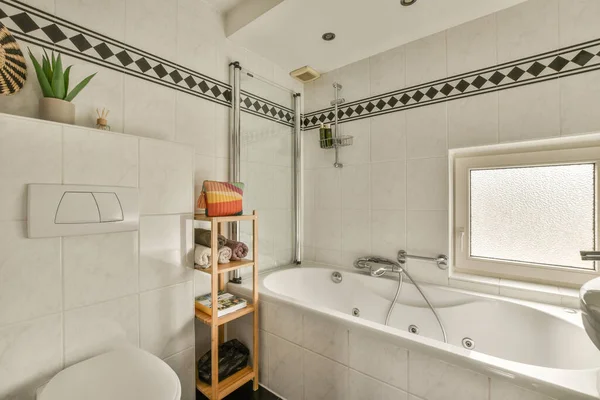 壁には白と黒のタイルの浴室と浴槽の横には木の棚があり — ストック写真