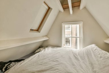 Odanın köşesinde bir yatak, bir tarafında açık bir pencere, diğer tarafında beyaz bir battaniye.