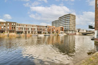 Bazı binalar ve tekneler üzerinde mavi gökyüzü olan büyük bir su kütlesinin önünde suyun üzerinde.