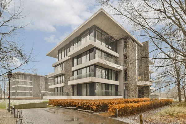 stock image a modern house in the middle of a park with trees and bushes on either side of the building there is an orange flower bed