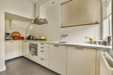 Bulaşık makinesinin bu fotoğrafta lavabo olarak kullanılabileceği beyaz dolapları ve tezgahı olan bir mutfak.