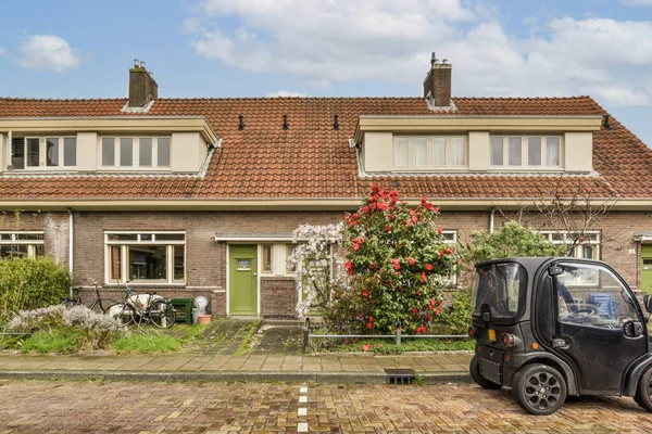 stock image a house with a small car parked in the driveway next to it and some flowers growing on the side of the road