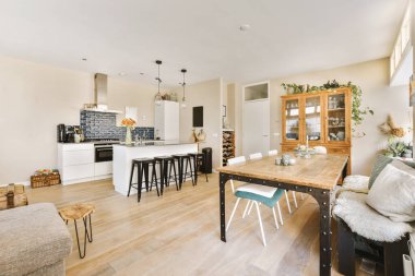 Ahşap zemin, beyaz duvarlar, ahşap döşemeler ve geniş pencereli bir dairede mutfak ve oturma odası.