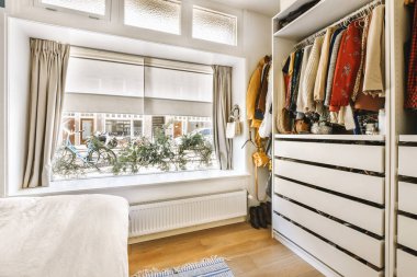 Duvarında giysiler asılı bir yatak odası ve sağında da bir pencere. Hemen yanında bir yatak var.