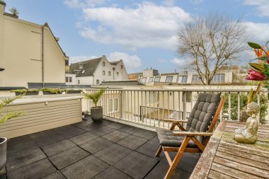 Ön tarafında sandalyeler ve çiçekler olan bir balkon. Evin sağ tarafında pencereli bir alan.