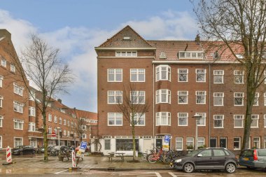 Park yerinde arabaları olan bir yerleşim yeri ve yan yolda yürüyen insanlar apartmanlarına doğru yürüyorlar.