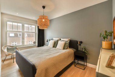 Yatağı, masası ve penceresi olan bir yatak odası sağ köşede yatak başlığının üstünde bir lamba var.