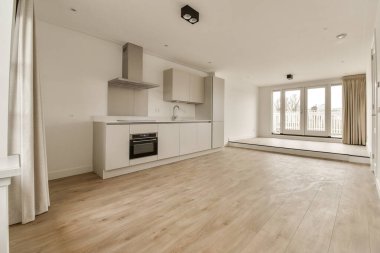 Odanın her iki tarafında ahşap döşemeleri ve beyaz dolapları olan boş bir oturma odası var.