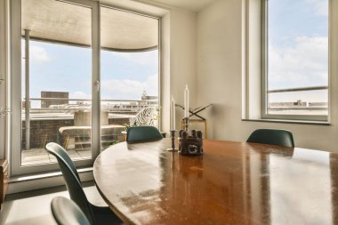 İçeriden çekilen şehir manzarasına bakan geniş pencereli bir odada bir masa ve sandalyeler.