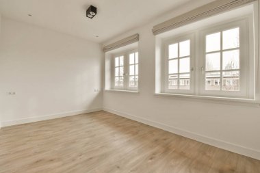 Beyaz duvarları ve ahşap döşemeleri olan boş bir oda. Pencerenin önündeki duvarda bir lamba var.