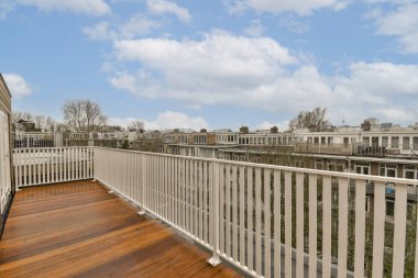Ahşap zeminli bir balkon ve evin yan tarafında beyaz korkuluklar var.