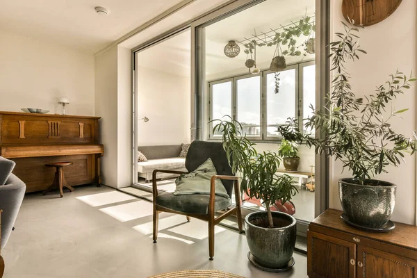 屋外のパティオにつながるガラスのドアの前に植物や椅子のあるリビングルーム — ストック写真
