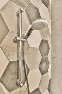 Arkasındaki duvarda altıgen kiremitli bir duş ve köşede de el ele tutuşan bir duş başlığı.