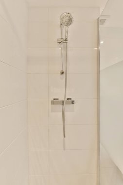Küvetin köşesinde duş başlığı ve parmaklığı olan bir banyo duvarda beyaz fayanslar var.