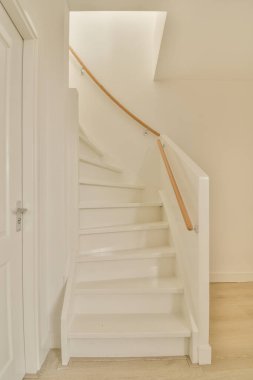 Ortasında merdiven, altında ahşap döşeme, beyaz duvarlar ve ahşap korkuluklar olan boş bir oda.