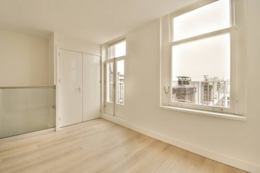 Beyaz duvarları ve ahşap döşemeleri olan boş bir oda. Dışarıdaki şehre bakan bir pencere var.