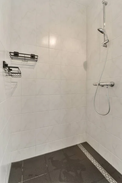 壁には白いタイルと黒い床があるシャワー室手のシャワーヘッドがあります — ストック写真