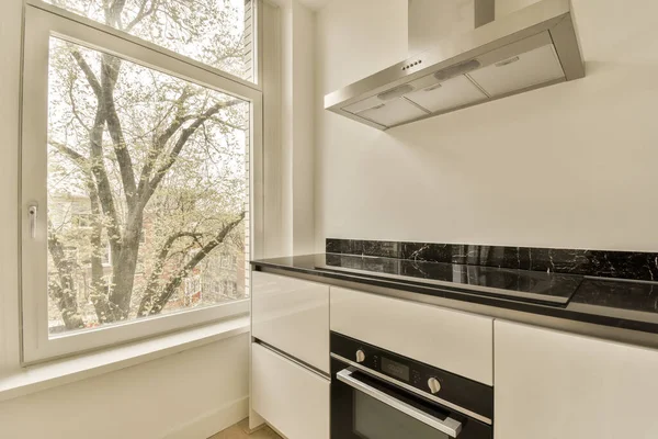 Penceresinde fırın ve soba olan bir mutfak. Sokakları çevreleyen ağaçlara bakıyor.