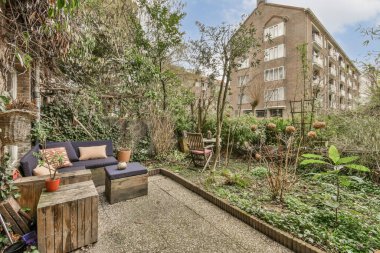 Ağaçlarla çevrili bir apartmanın önünde bir sürü çiçek ve bitki olan bir arka bahçe.