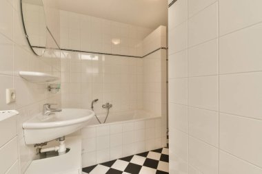 Yerde siyah beyaz kareli bir banyo, duş kabininde lavabo ve ayna.