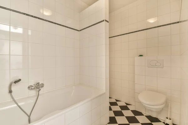 床に黒と白のタイル張りの白いバスルームと角にあるトイレ — ストック写真