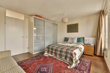 Duvarın köşesinde yatak odası, kanepe ve gardırop olan bir yatak odası kullanılabilecek bir halı.