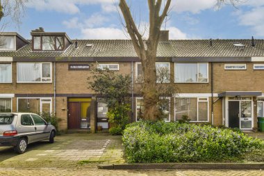 Garaj yolunda arabaları olan bazı evler ve evin her iki tarafında ağaçlar var. Bir araba yan yana park edilmiş.