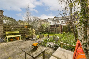 Arka bahçesinde sandalyeler, masalar ve bitkiler olan eski bir tuğla duvarın önünde.