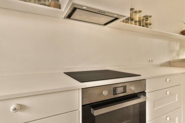 Beyaz dolapları olan bir mutfak ve arkasında da vazoda bir saksı çiçek olan bir fırın.