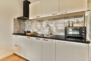 Bu fotoğrafta tezgahların üzerinde beyaz dolaplar ve siyah tezgahlar olan bir mutfak içeriden çekilmiş.