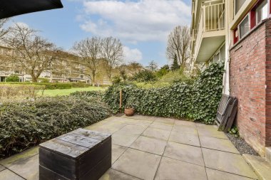 Dışarıda, çalılarla çevrili tuğla bir binanın önünde bazı bitki ve kutuların olduğu bir yer.