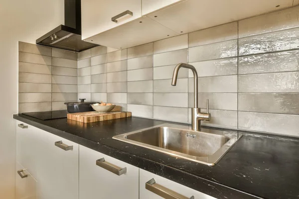厨房后面是一个有黑色台面和白色瓷砖的厨房 后面是一个不锈钢水龙头 — 图库照片