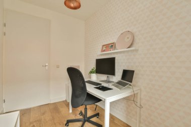 Masası, sandalyesi ve bilgisayarı olan bir oda beyaz duvar kağıdının önünde.