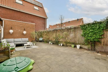 Arka bahçesinde bir kanepe ve arkasında kırmızı tuğla bir duvarın önünde bitkiler olan bir yer.