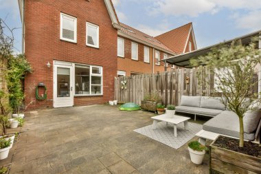 Ön tarafında mobilya ve bitkiler olan bir dış alan. Görüntü içeriden alınıyor ama kimse onu göremiyor.