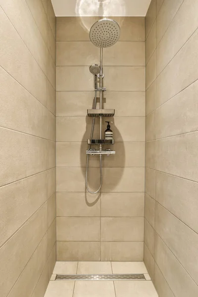壁にはタイル張りのシャワー室とベージュのタイルがあり手押しのシャワーヘッドがあります — ストック写真