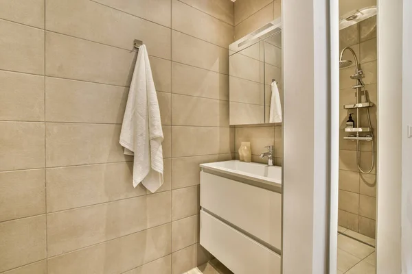 stock image a bathroom with beige tiles and white towel hanging on the wall next to the bathtub in the shower room