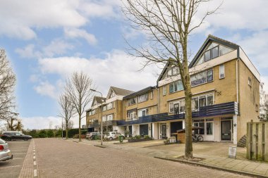 Binanın önüne park edilmiş evler ve arabalarla dolu bir cadde solda boş bir otopark var. Binalara tuğla örülmüş.