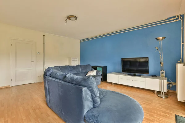 a living room with blue walls and hardwood flooring, including a large couch in front of the tv set