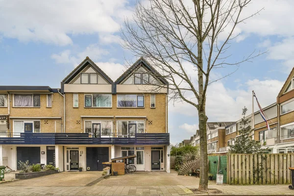 Boş bir sokak, önünde evler ve ağaçlar var. Caddenin karşısından sağa doğru fotoğraf çekiliyor.