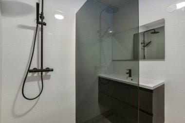 Duvarlarında siyah beyaz fayanslar olan modern bir banyo. Aynanın köşesine monte edilmiş bir duş başlığı da dahil.