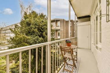 Masası ve sol tarafında sandalyeleri olan bir balkon, uzaktaki sokağa bakıyor.