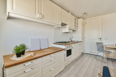 Adanın üzerinde beyaz dolapları ve ahşap tezgahları olan bir mutfak nasıl yaşadığımıza bir örnektir.