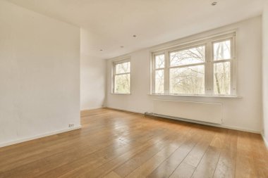 Odanın dışındaki ağaçlara bakan ahşap döşemeli ve geniş pencereli boş bir oda beyazdır.