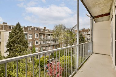 Arka planda ağaçlar ve binalar olan bir balkon. Bir apartmanın penceresinden alınmış.