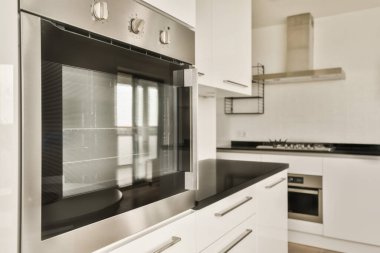 Merkezi elektrikli fırın da dahil olmak üzere duvarında beyaz dolaplar ve siyah tezgahlar olan modern bir mutfak.