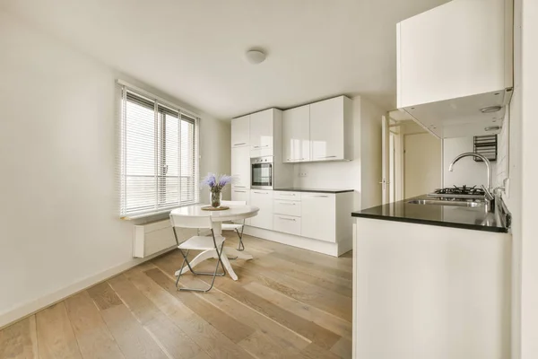 Kuchnia Jadalnia Małym Mieszkaniu Białymi Szafkami Drewnianą Podłogą Czarnymi Blatami — Zdjęcie stockowe