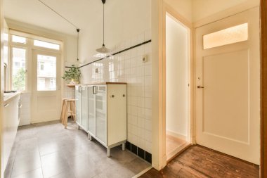 Duvarlarında beyaz fayanslar, kapılarında ahşap süslemeler olan bir evde mutfak ve yemek odası.