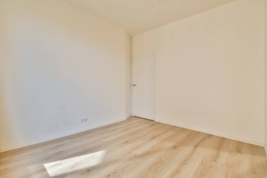 Ahşap zemini ve beyaz duvarları olan boş bir oda. Köşede başka bir odaya açılan bir kapı var.